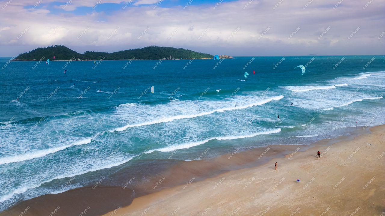 Campeche em Florianópolis com vista aérea da praia, kitesurfistas, vegetação densa e céu nublado