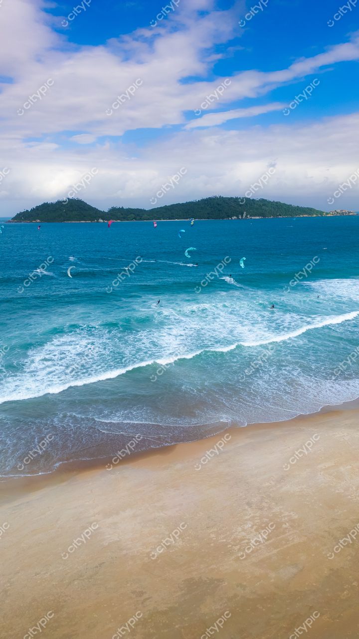 Campeche em Florianópolis com mar azul vibrante, kitesurfistas e céu misto durante o dia em paisagem tranquila