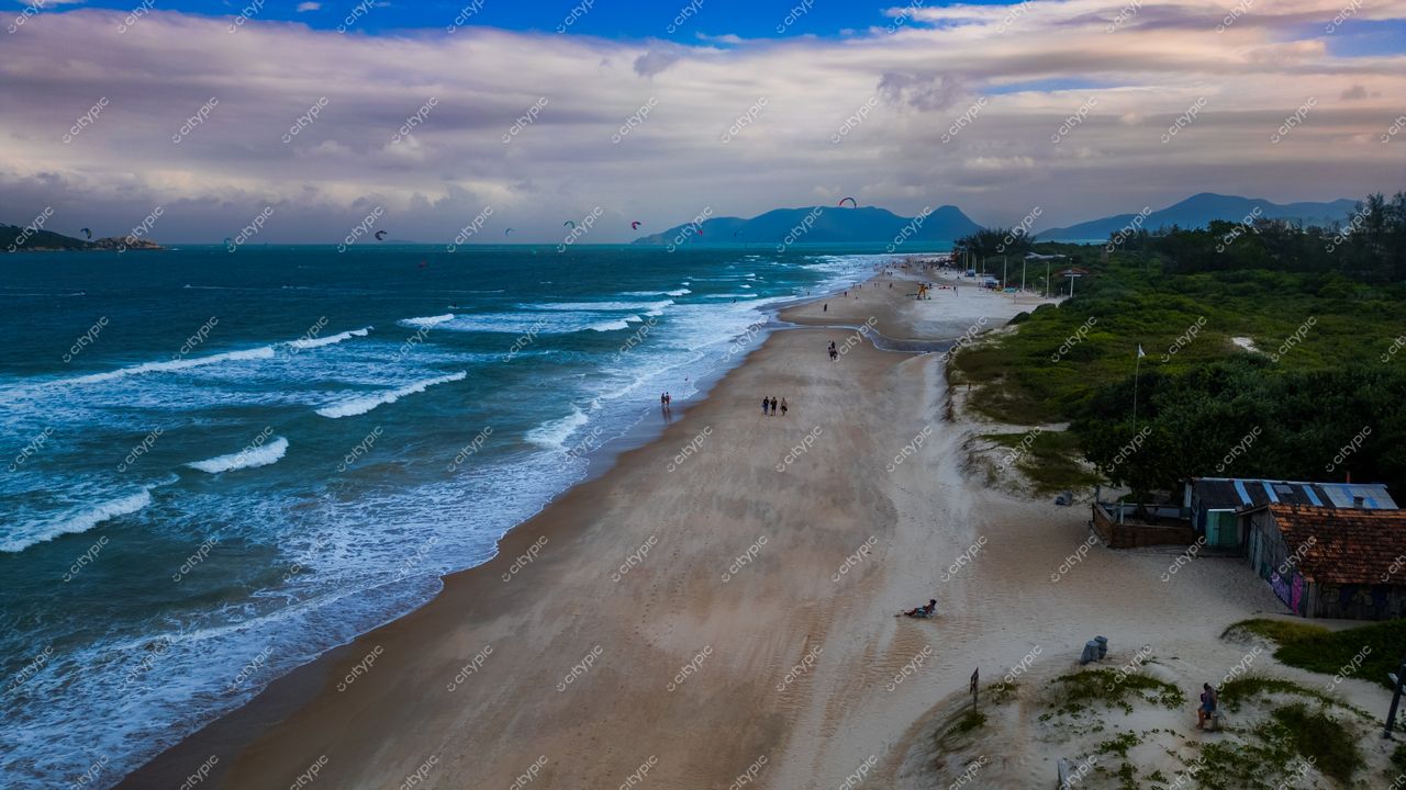 Campeche em Florianópolis com kitesurfistas ao longe e vegetação ao fundo durante o final da tarde