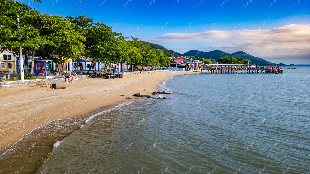 Ribeirão da Ilha em Florianópolis com praia de areia clara, píer de madeira e casas coloridas sob luz natural