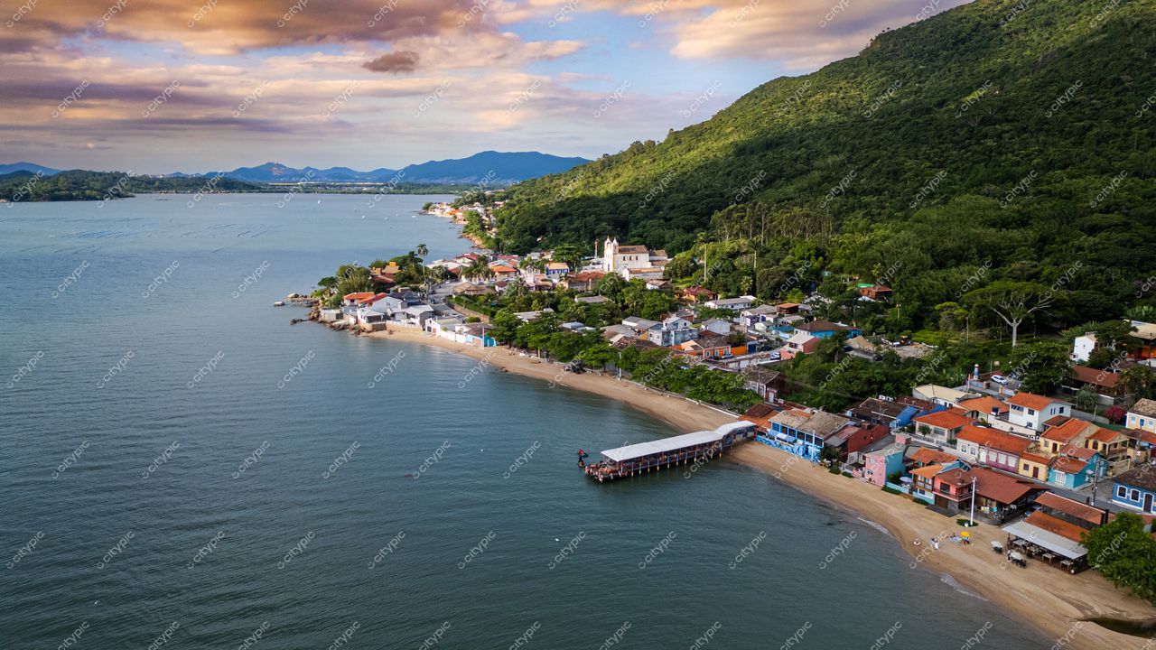 Ribeirão da Ilha em Florianópolis com vista aérea ao entardecer, casas coloridas e vegetação exuberante ao fundo