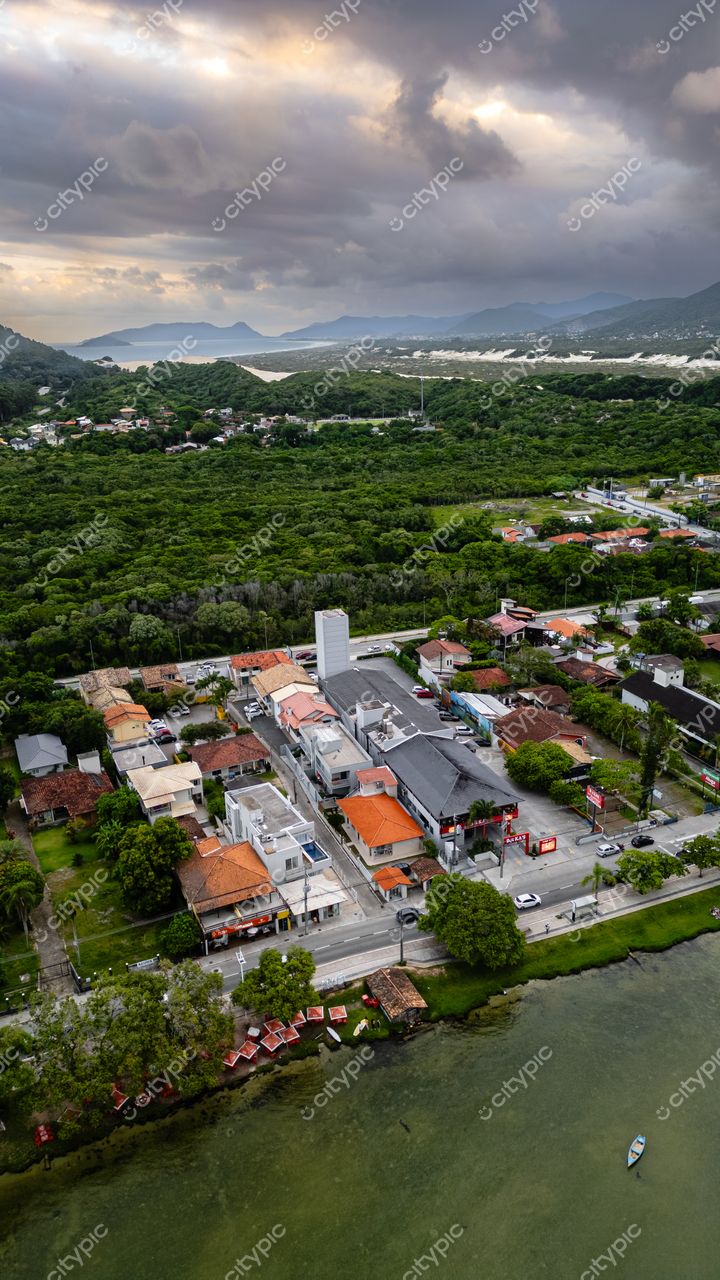 Rendeiras em Florianópolis com casas coloridas, vegetação densa e montanhas sob céu nublado em vista aérea