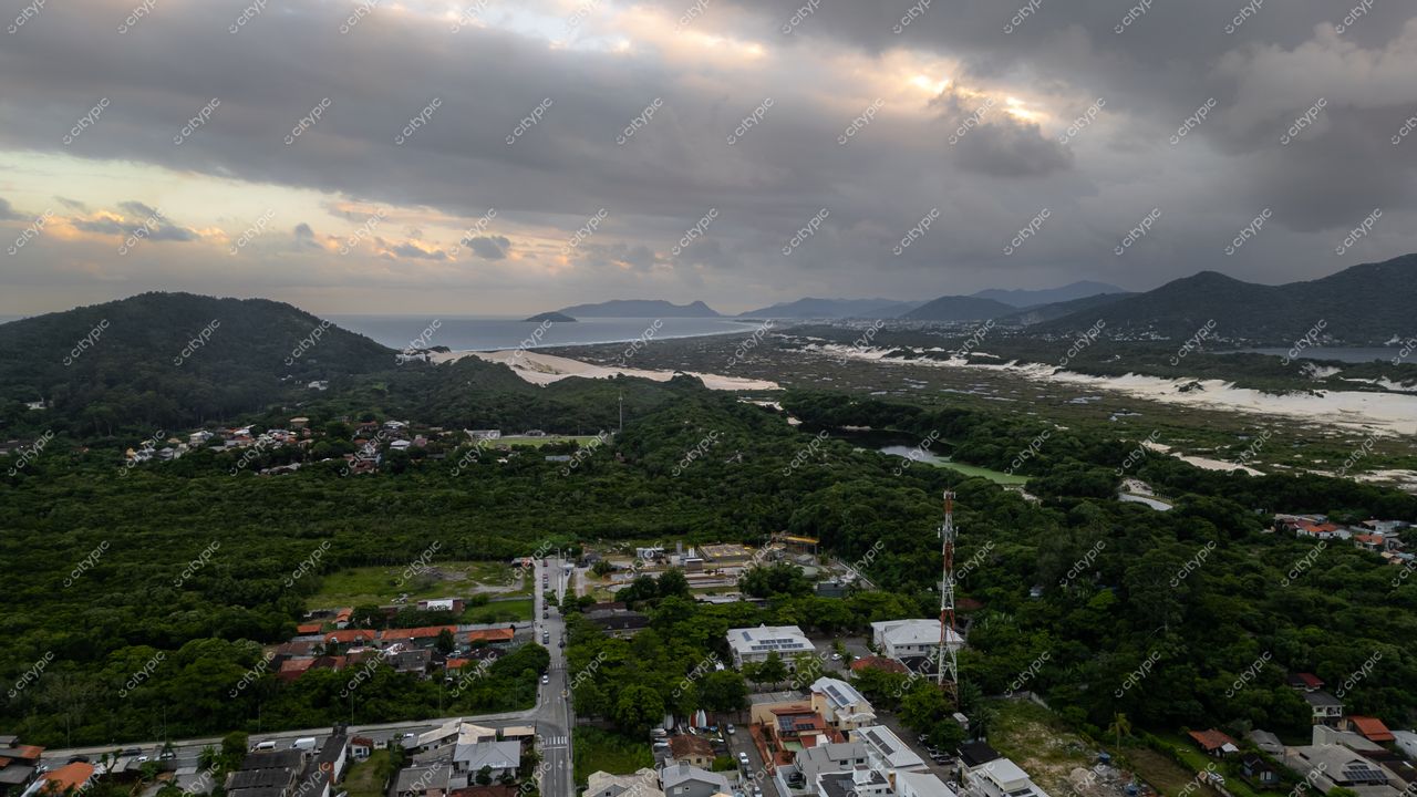 Rendeiras em Florianópolis com montanhas ao fundo, vegetação densa e céu nublado sobre a faixa de areia clara