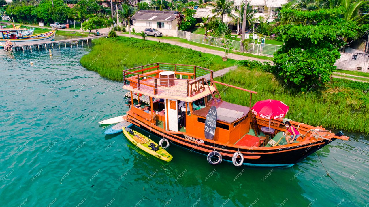 Florianópolis, Santa Catarina, barco colorido ancorado em águas calmas com vegetação e casas ao fundo durante o dia