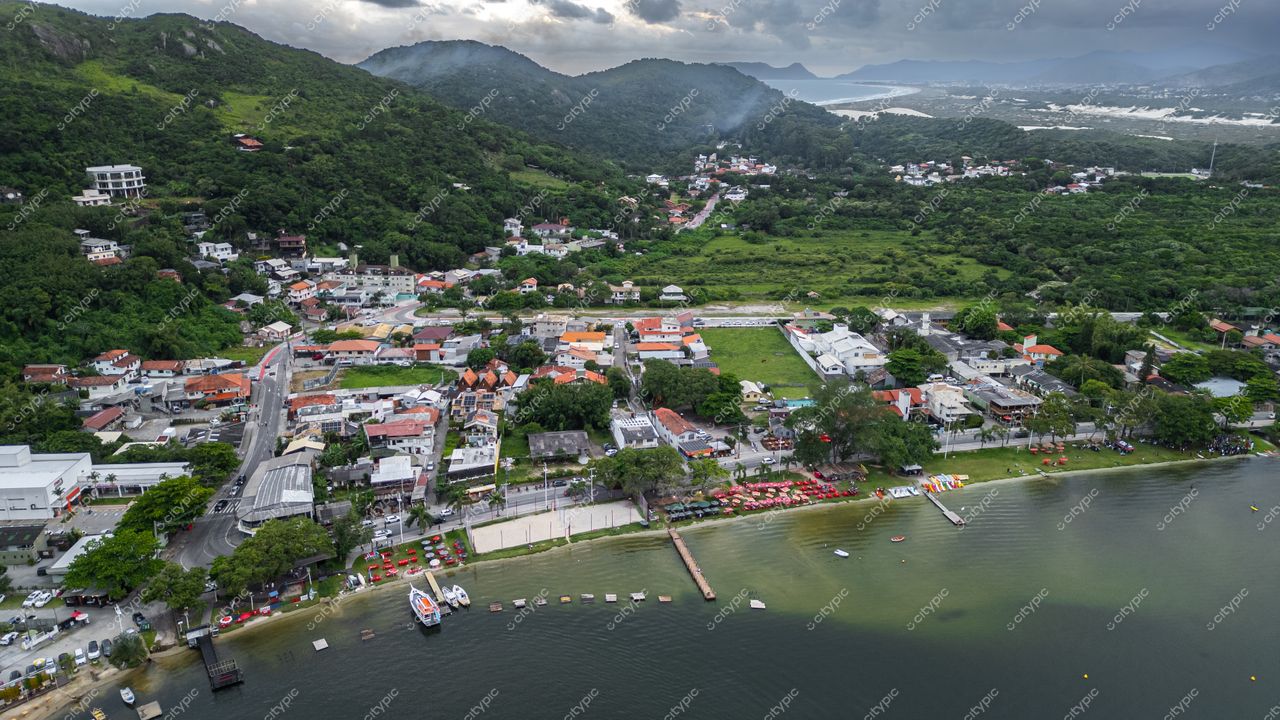 Rendeiras em Florianópolis com vista aérea de casas coloridas, montanhas verdes e praia tranquila sob céu nublado