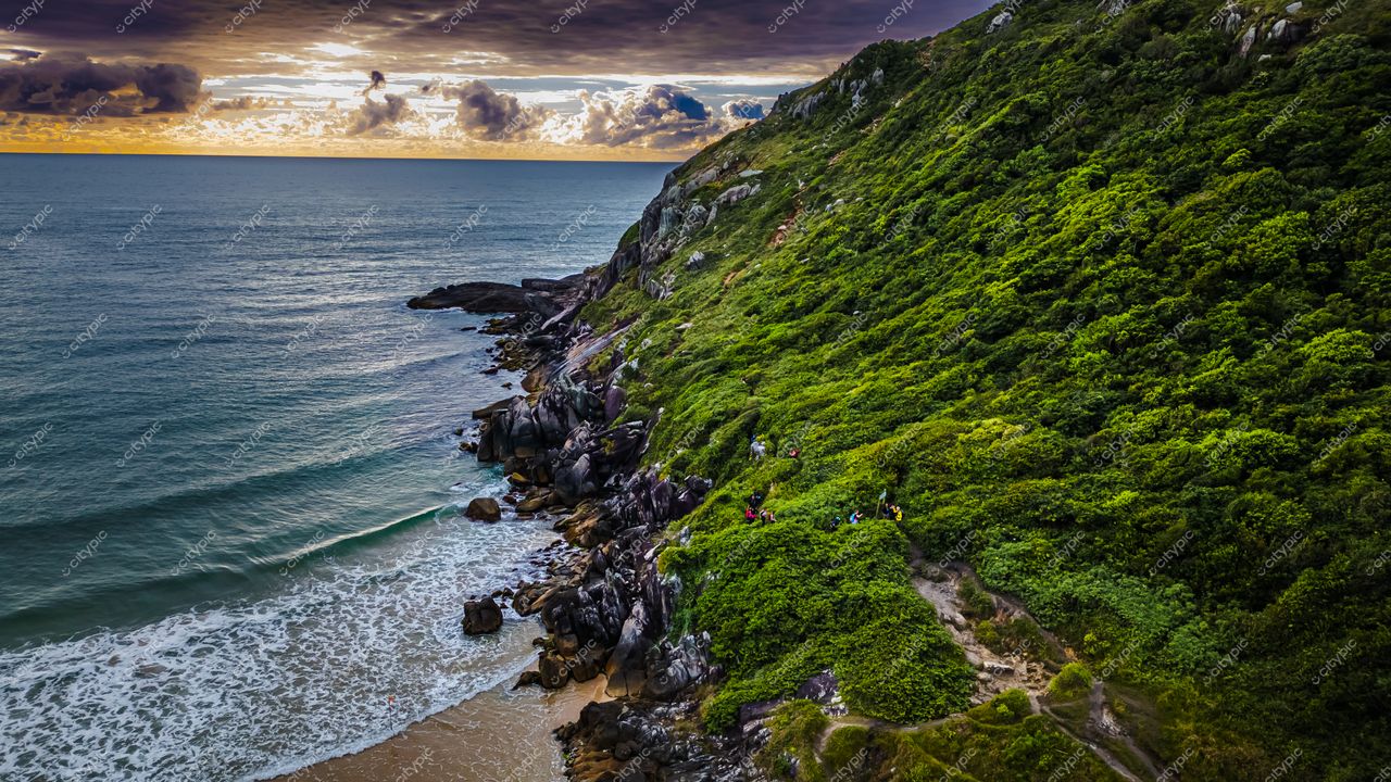 Lagoinha do Leste em Florianópolis com vegetação densa, mar calmo e céu parcialmente nublado ao pôr do sol