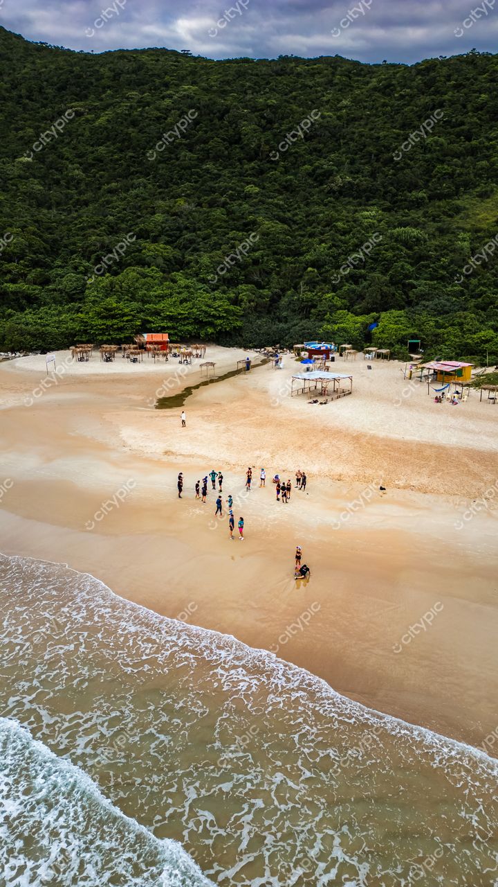 Lagoinha do Leste em Florianópolis com vegetação densa, céu nublado e pessoas na areia clara da praia