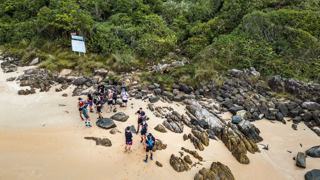 Lagoinha do Leste em Florianópolis com grupo de pessoas conversando em praia sob céu nublado e vegetação densa