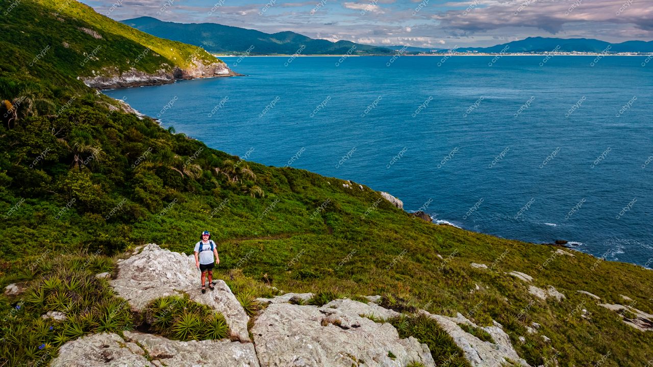 Lagoinha do Leste em Florianópolis com homem sobre pedras e vegetação verde, mar azul e montanhas ao fundo