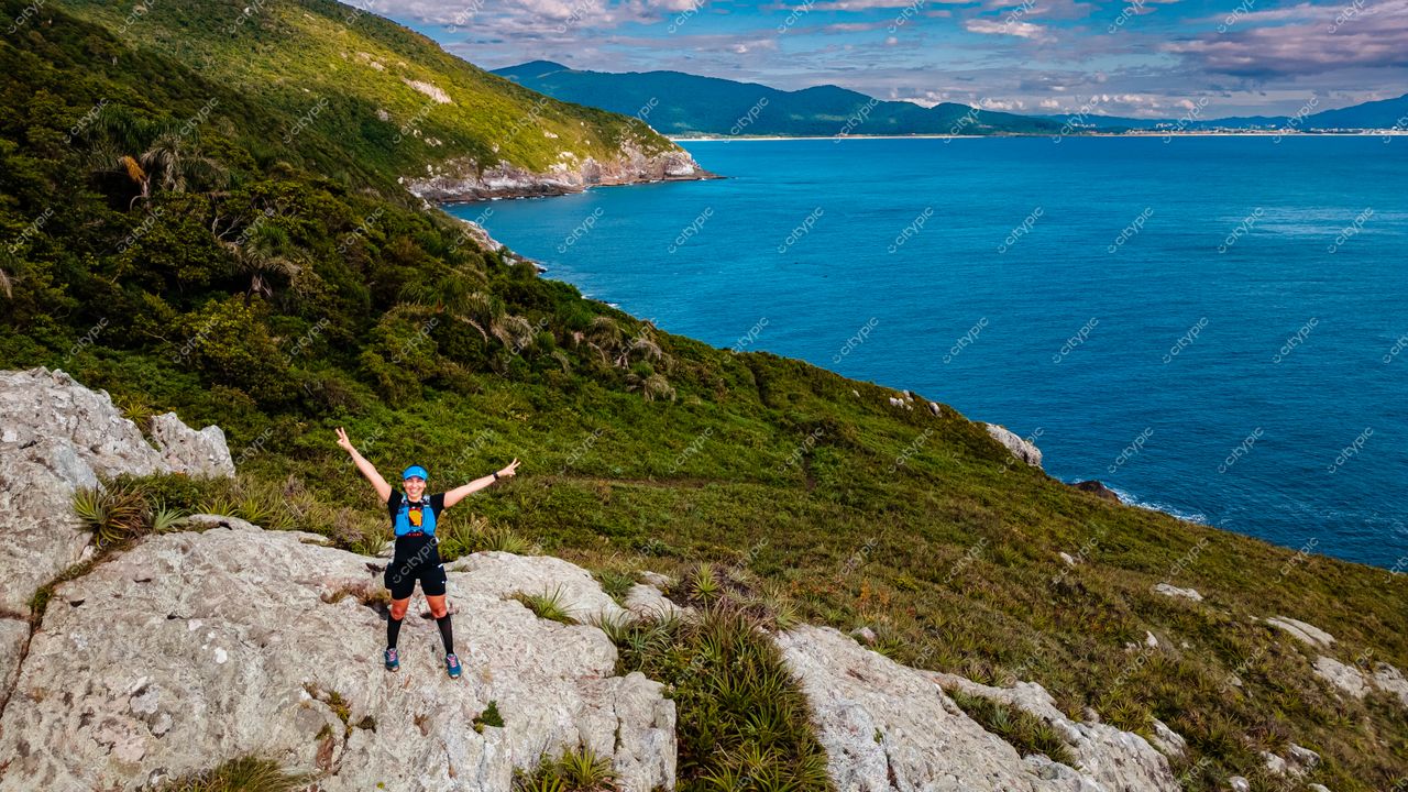 Lagoinha do Leste em Florianópolis com trilheiro em rocha elevada e vegetação verde sob céu parcialmente nublado