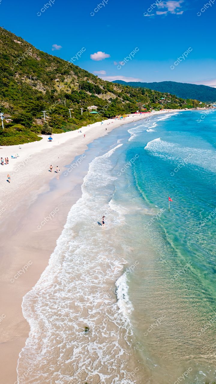 Lagoinha do Leste em Florianópolis com mar azul, areia clara e vegetação densa sob céu ensolarado e nuvens esparsas