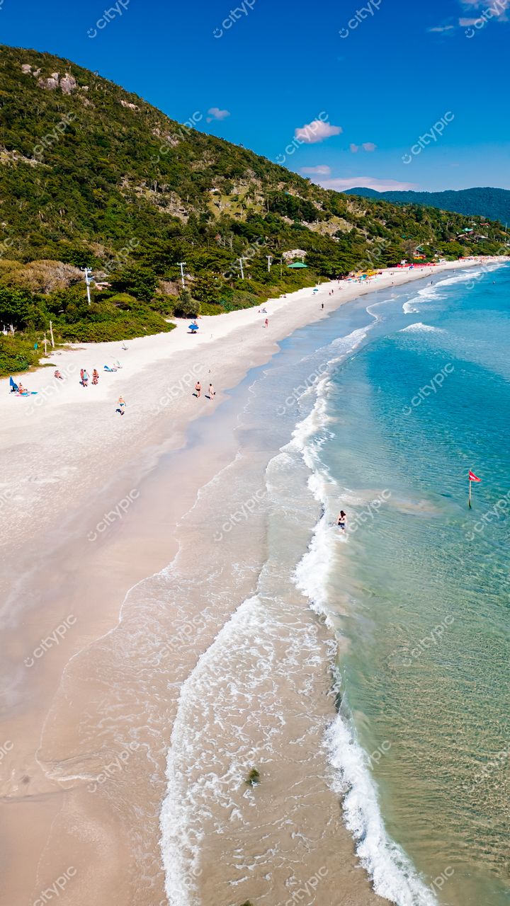 Lagoinha do Leste em Florianópolis com areia clara, águas turquoise e vegetação densa sob céu azul e nuvens