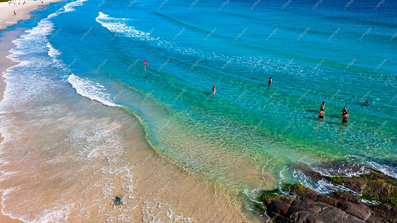 Lagoinha do Leste em Florianópolis com águas azul-turquesa e pessoas entrando no mar sob intensa luz solar