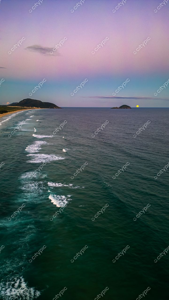 Praia do Moçambique em Florianópolis com mar calmo, céu em gradientes de rosa e azul e lua ao fundo