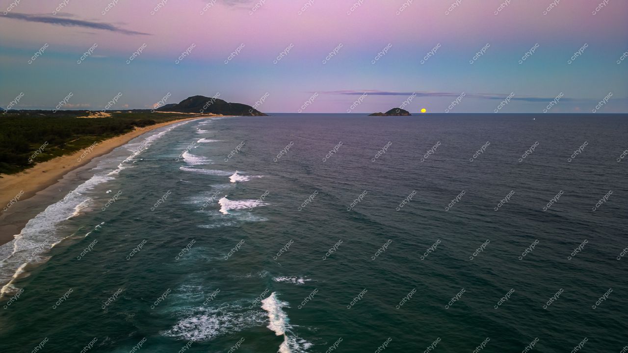 Praia do Moçambique em Florianópolis com areia clara e mar azul durante o crepúsculo, montanhas ao fundo