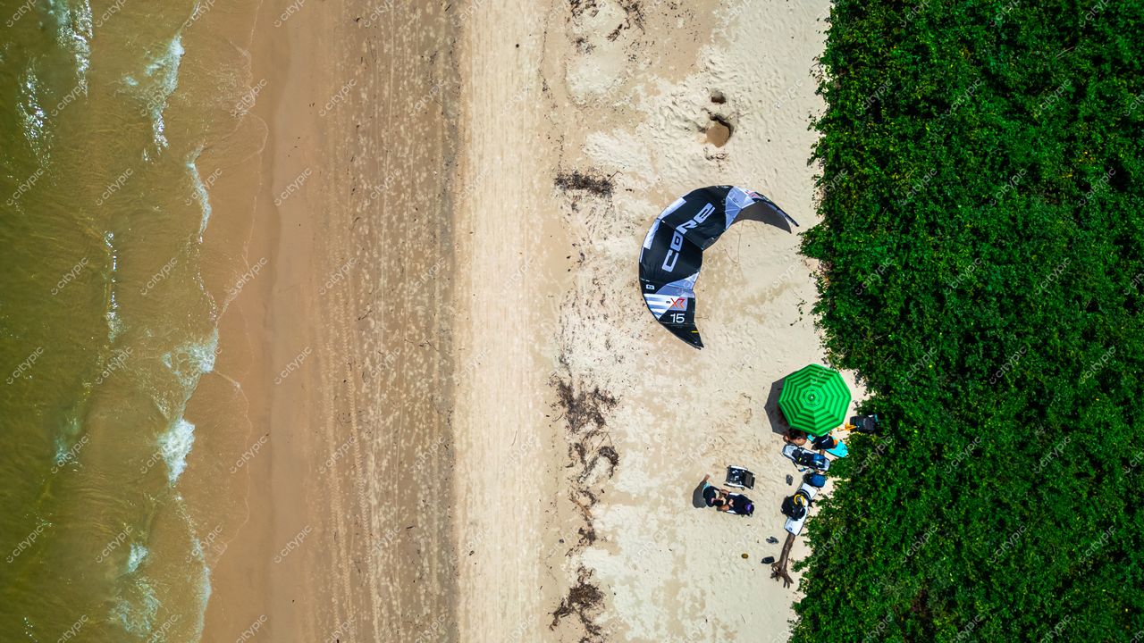 Praia da Daniela em Florianópolis com vegetação densa e kite preto ancorado na areia em dia ensolarado