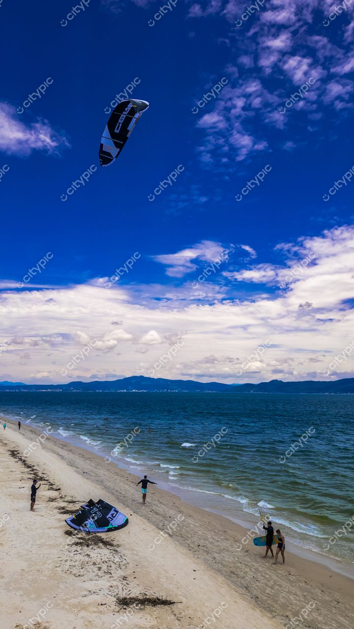 Praia da Daniela em Florianópolis com céu azul, kitesurf no ar e pessoas na areia em dia ensolarado