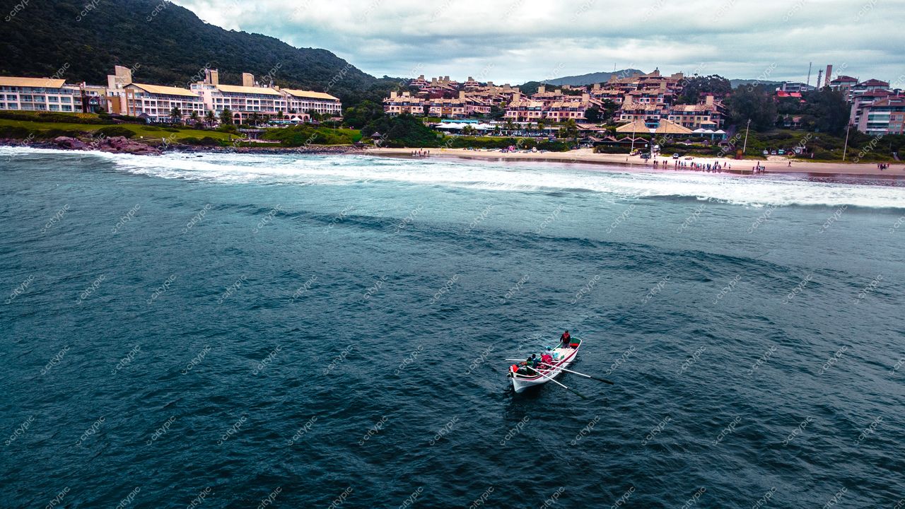 Florianópolis, Santa Catarina, vista costeira com barco à remo e construções em colina sob céu nublado