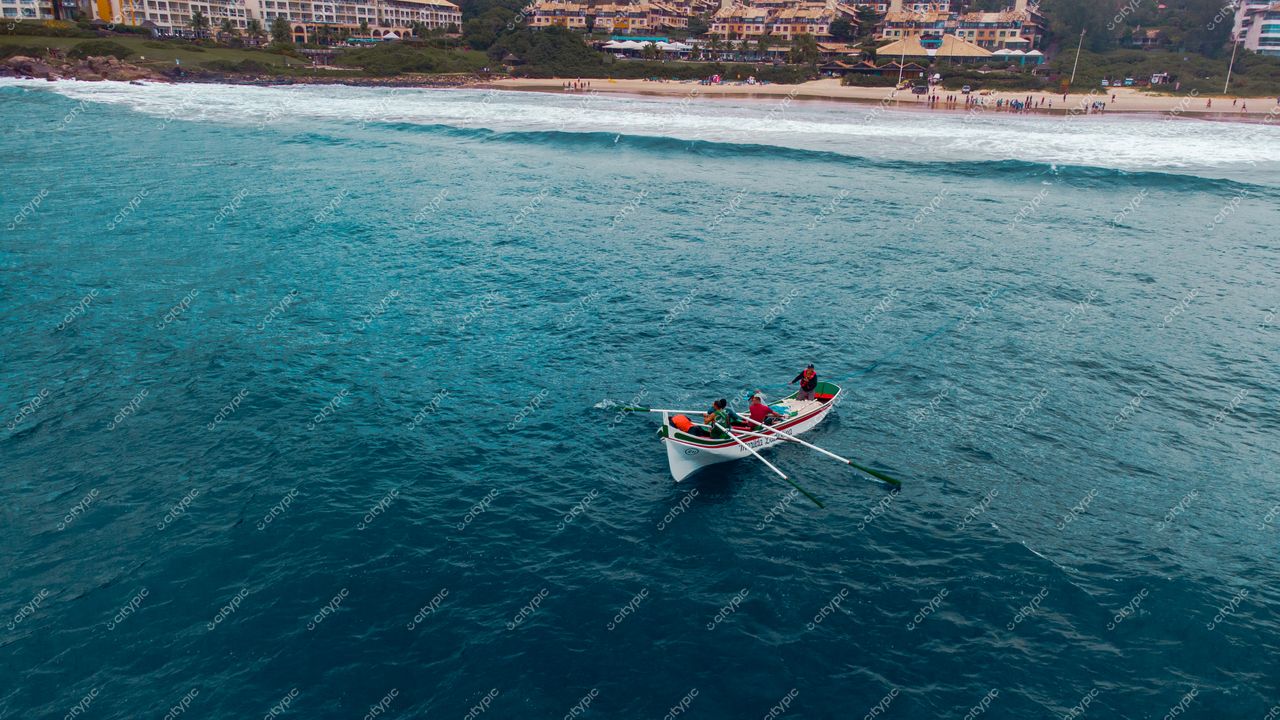 Florianópolis, Santa Catarina, barco ancorado em águas azul-turquesa com praia e prédios ao fundo em dia nublado