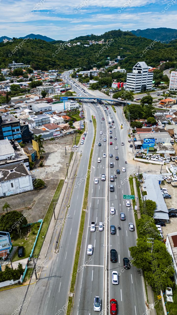 Hospital SOS Cárdio em Florianópolis com vista aérea de via movimentada, vegetação densa e céu claro com nuvens dispersas