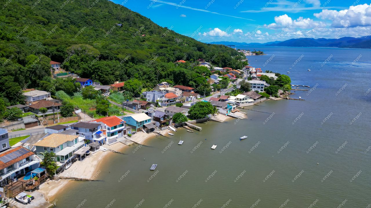 Ribeirão da Ilha em Florianópolis com casas coloridas, vegetação verde e embarcações ancoradas em dia ensolarado