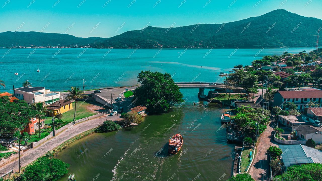 Florianópolis, Santa Catarina vista aérea de área costeira com canal navegável e montanhas ao fundo em dia ensolarado