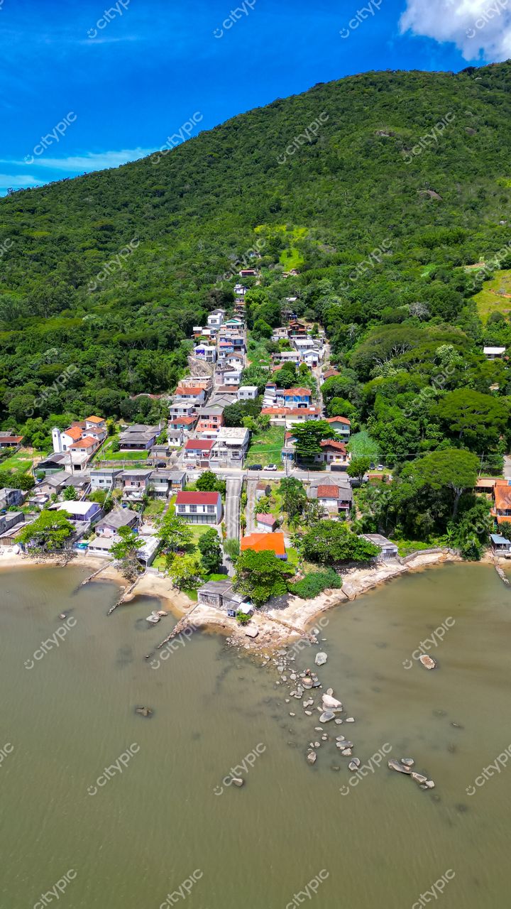 Ribeirão da Ilha em Florianópolis com vista aérea de residências em encostas verdes e praia de pedras sob luz natural
