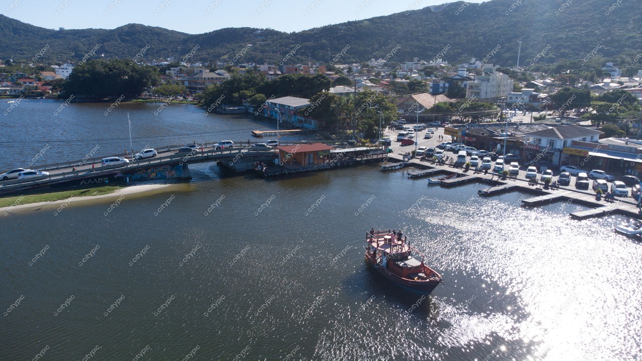 Florianópolis, Santa Catarina vista aérea com barco ancorado, vegetação montanhosa e acesso viário movimentado em dia ensolarado