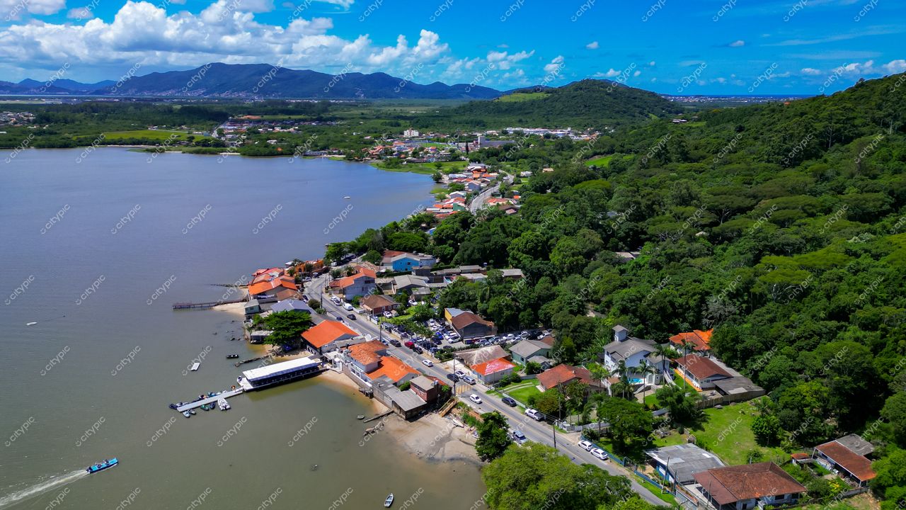 Ribeirão da Ilha em Florianópolis com vista aérea de vegetação densa, casas coloridas e céu claro em dia ensolarado