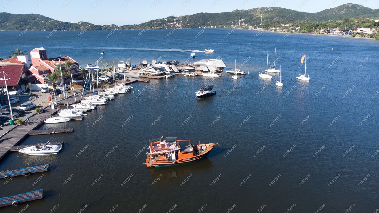 Florianópolis, Santa Catarina, barco de madeira navegando em porto com montanhas ao fundo e luz natural intensa