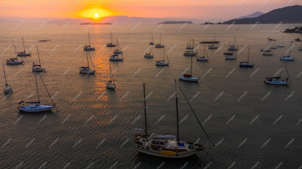 Florianópolis, Santa Catarina, pôr do sol alaranjado refletido na baía com veleiros ancorados e montanhas ao fundo