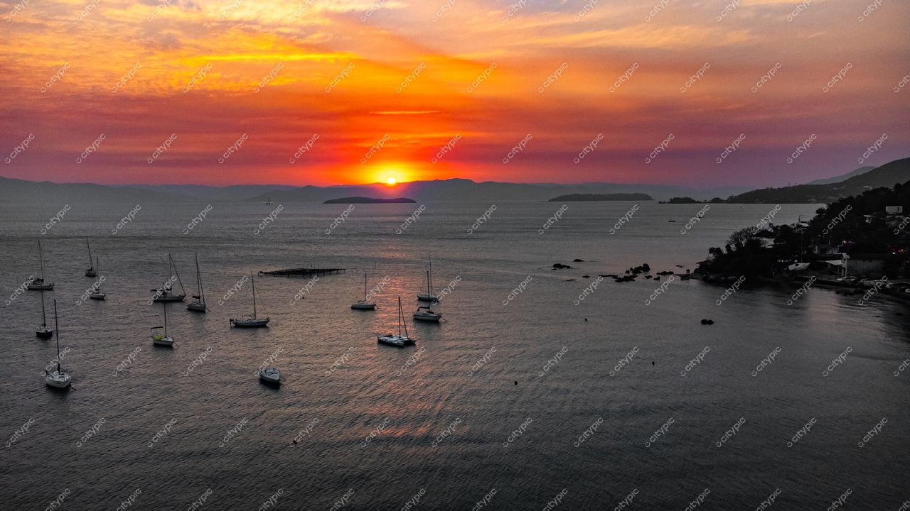 Florianópolis, Santa Catarina, pôr do sol vibrante sobre a baía com barcos à vela e área urbanizada ao fundo