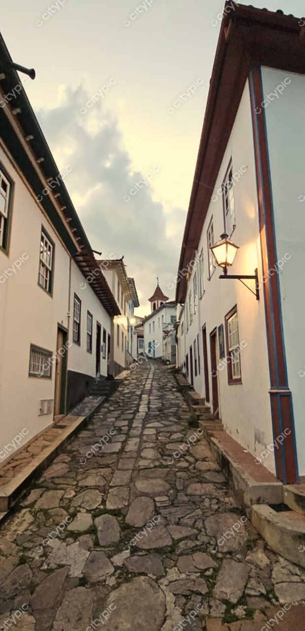 Diamantina, Minas Gerais, rua de paralelepípedos com casas coloniais brancas ao entardecer e céu nublado