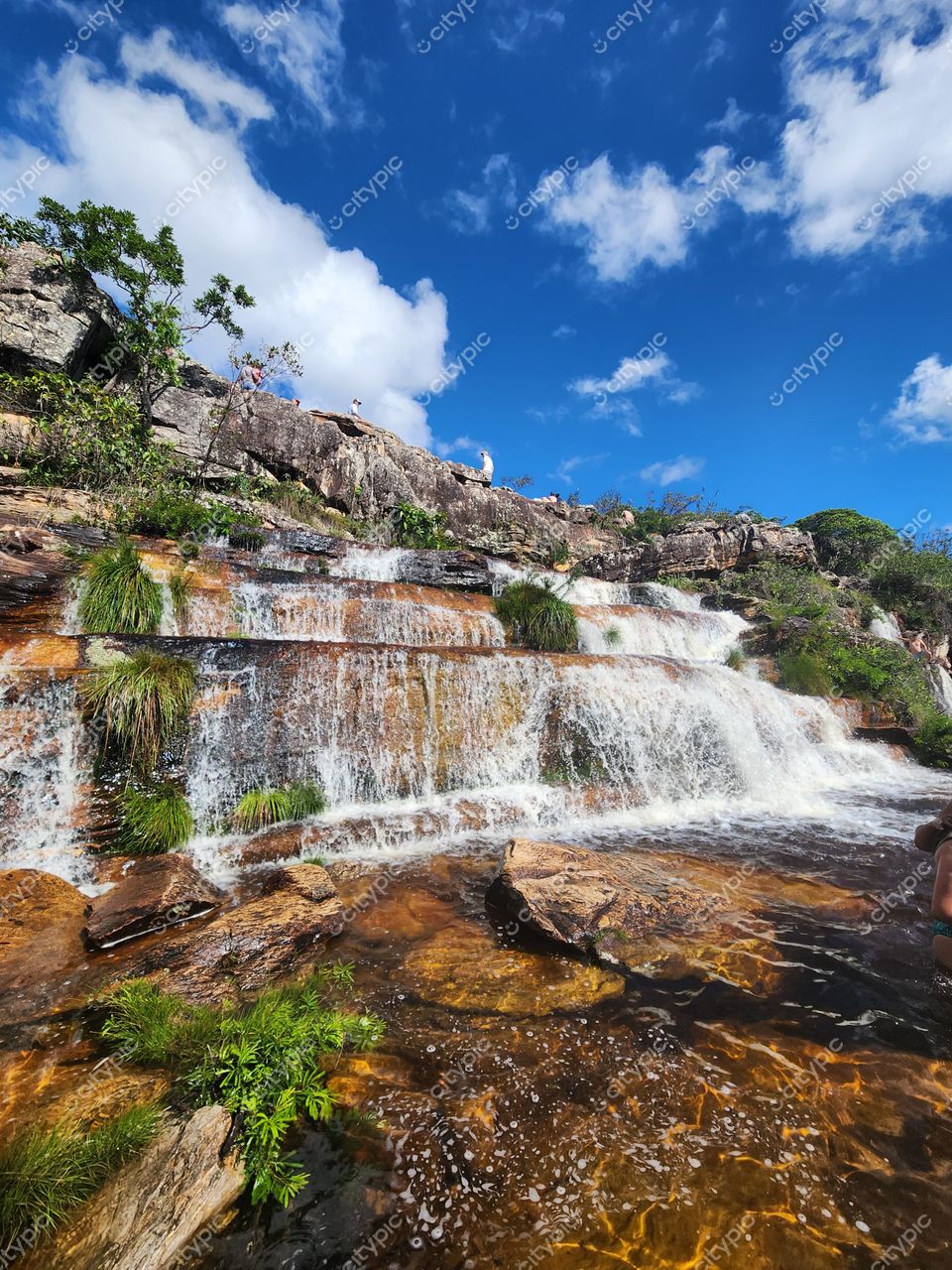 Diamantina, Minas Gerais, cachoeira em camadas com vegetação exuberante e céu azul com nuvens brancas
