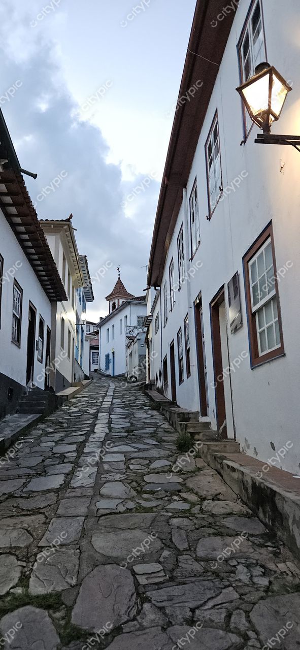 Diamantina, Minas Gerais, rua de paralelepípedos com casas coloniais e torre ao fundo sob céu nublado
