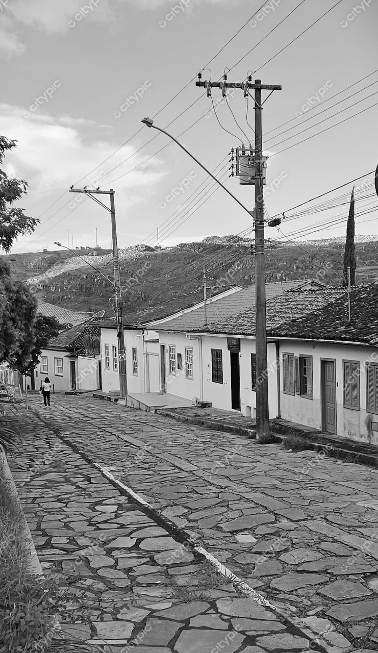 Diamantina, Minas Gerais, rua de paralelepípedos ao entardecer com vegetação e arquitetura colonial sob céu claro