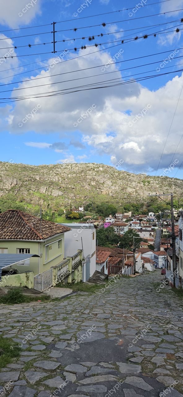 Diamantina, Minas Gerais, rua de paralelepípedos com casas coloridas e colina ao fundo sob céu nublado no final da tarde
