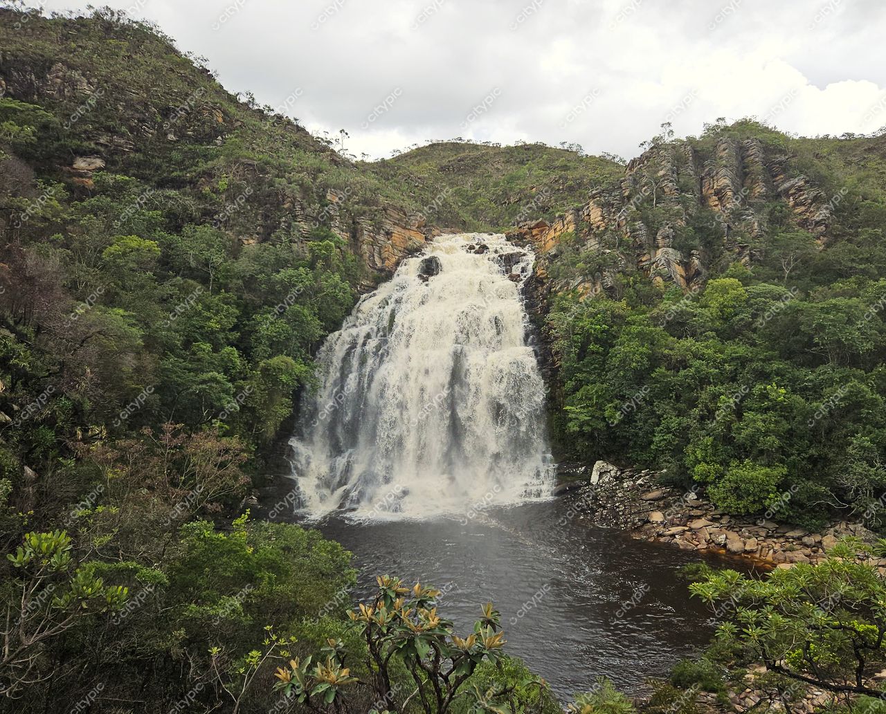 Santana do Riacho, Minas Gerais, cachoeira em várias camadas com lago tranquilo e vegetação densa sob céu nublado