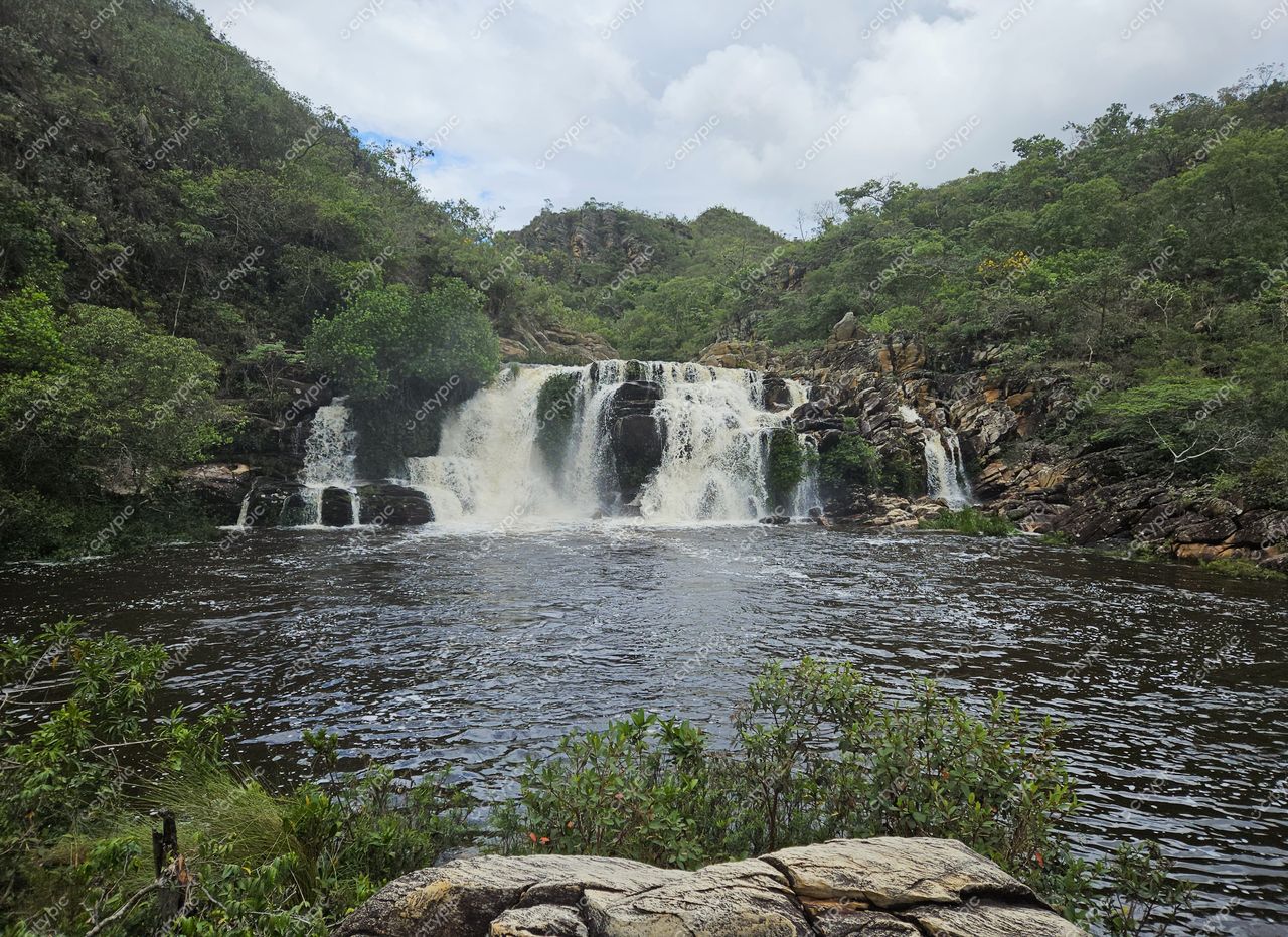 Santana do Riacho, Minas Gerais, cachoeira em camadas com vegetação densa e céu nublado em clima ameno