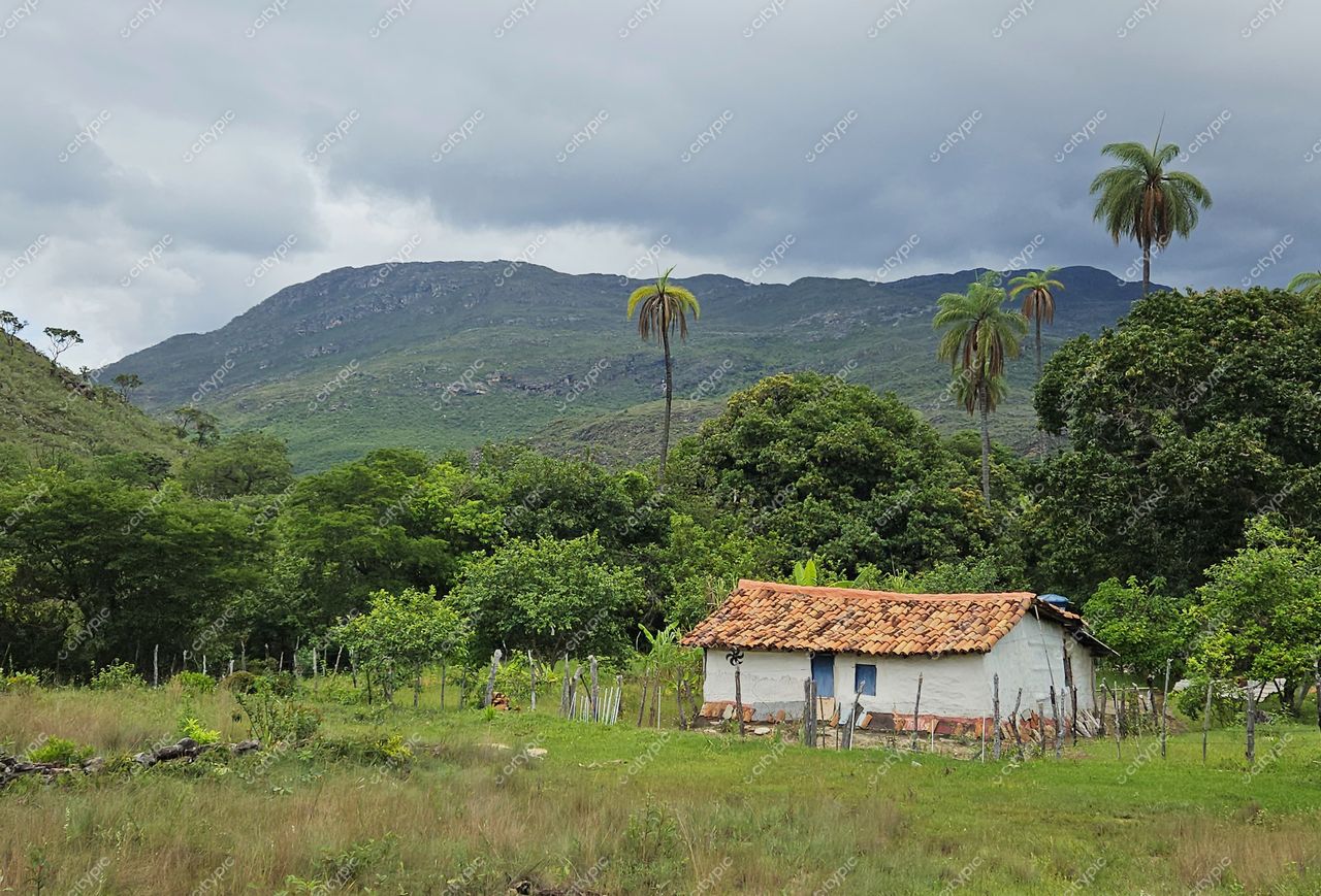 Santana do Riacho, Minas Gerais, casa rural com paredes brancas em meio a vegetação densa e montanhas ao fundo