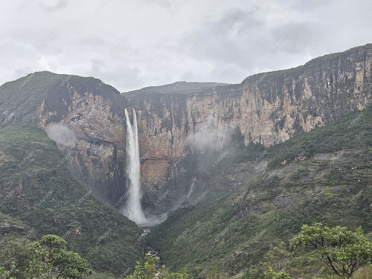 Conceição do Mato Dentro, Minas Gerais, cachoeira em vale com rochas íngremes e vegetação exuberante sob céu nublado