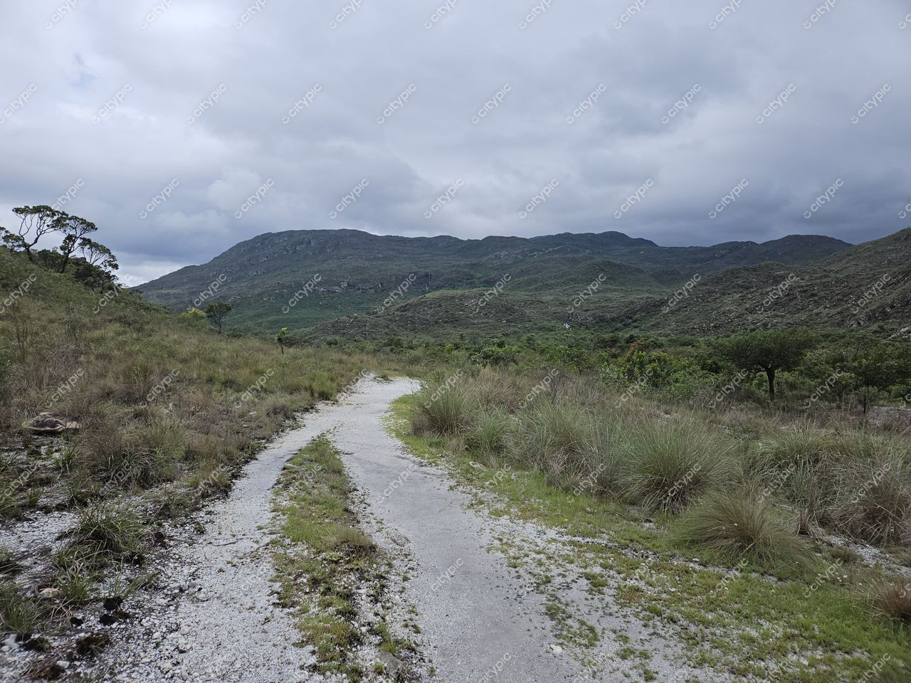 Conceição do Mato Dentro, Minas Gerais, trilha de terra e pedra em paisagem montanhosa com vegetação rasteira e céu nublado