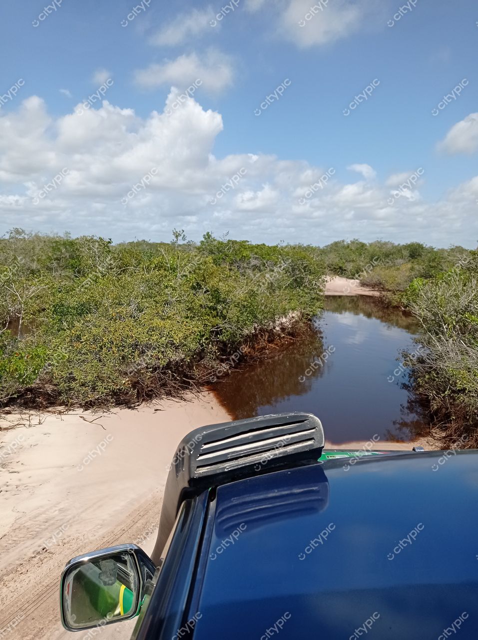 Barreirinhas, Maranhão vista panorâmica de caminho estreito cercado por vegetação e água com céu nublado e veículo off-road
