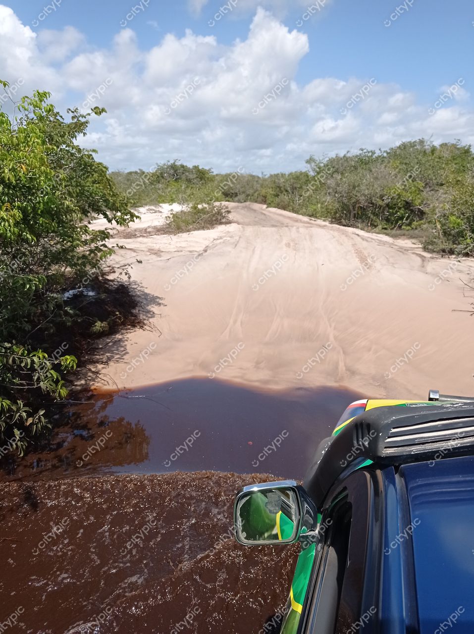 Barreirinhas, Maranhão, estrada de areia com veículo off-road próximo a poça d’água em dia ensolarado
