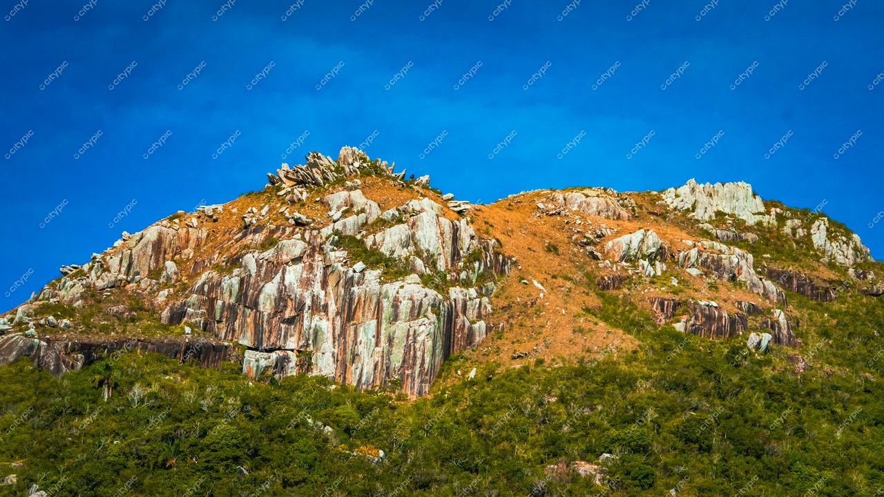 Lagoinha do Leste em Florianópolis com rochas cinza e laranja sob céu azul em dia ensolarado e vegetação densa