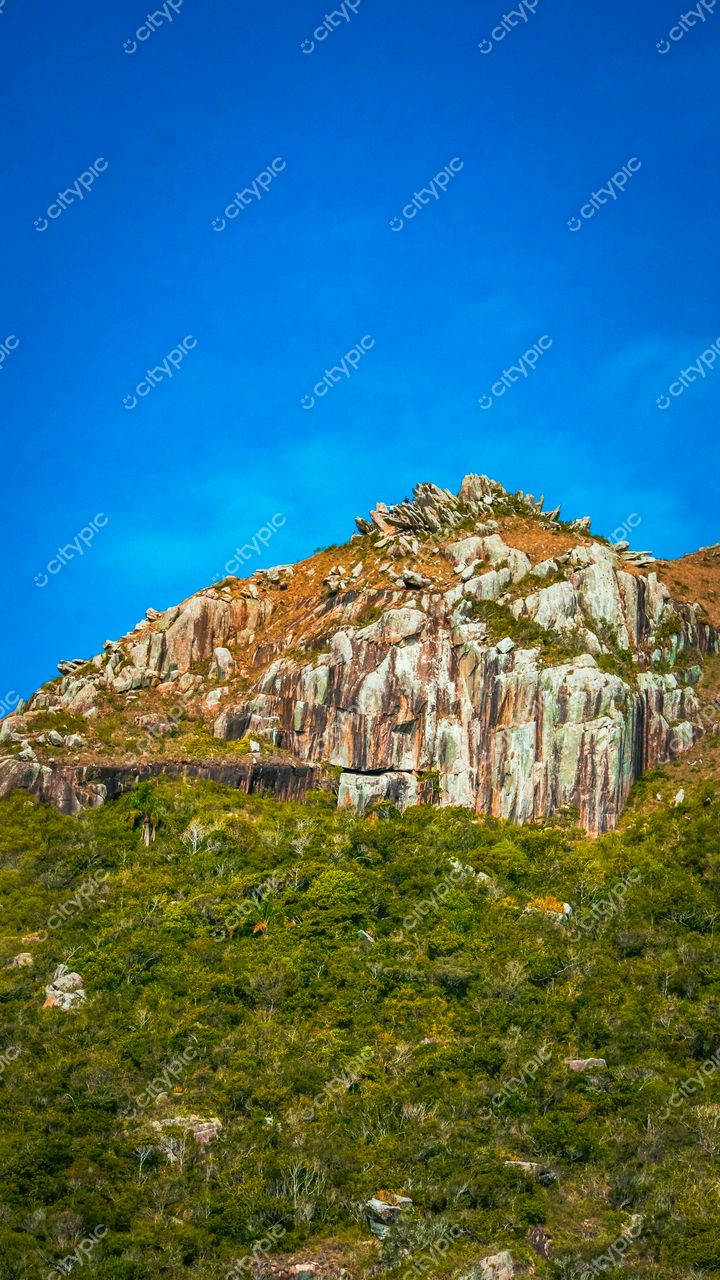 Lagoinha do Leste em Florianópolis com montanha de rochas cinzas e laranjas sob céu azul e vegetação verde