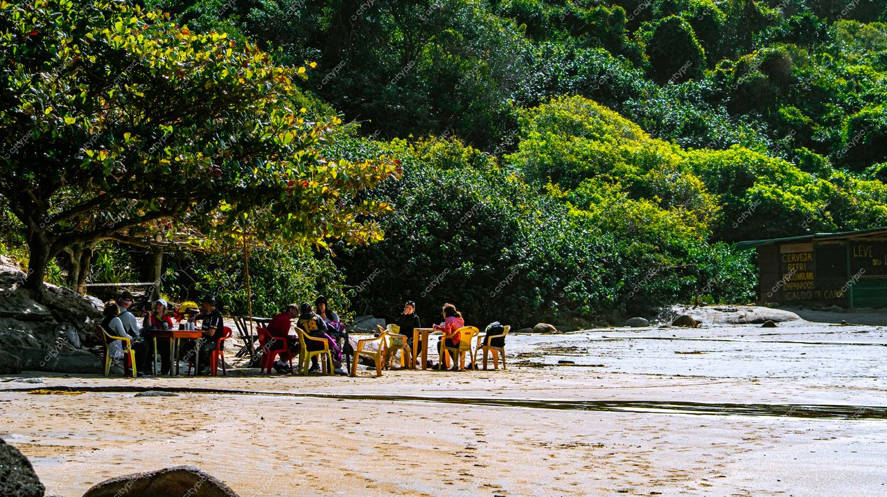 Lagoinha do Leste em Florianópolis com pessoas em cadeiras coloridas e mesas de madeira à beira da praia