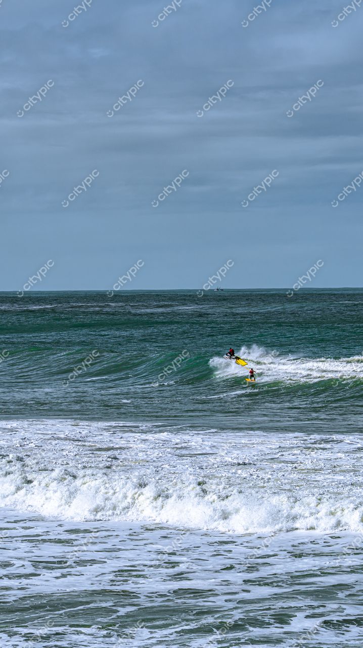 Lagoinha do Leste em Florianópolis com surfistas em ondas brancas sob céu nublado e vegetação ao fundo