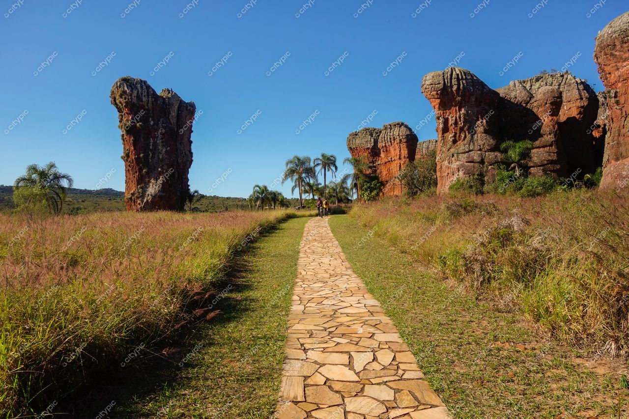 Ponta Grossa, Paraná, trilha pavimentada entre formações rochosas vermelhas e vegetação sob céu azul em dia ensolarado
