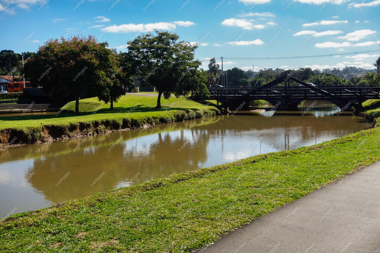 Curitiba, Paraná, cena tranquila do Parque Barigui com canal refletindo luz do dia e ponte de madeira